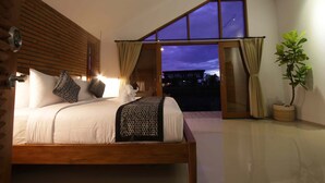 A bedroom with a large bed, a view of the night sky, and a potted plant. - Kubu Tropis (Ubud)