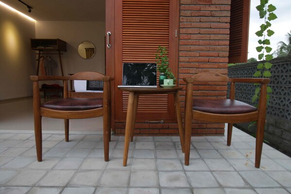 Deux chaises en bois avec des assises rembourrées et une petite table sur laquelle se trouvent un ordinateur portable et un pot de fleurs.