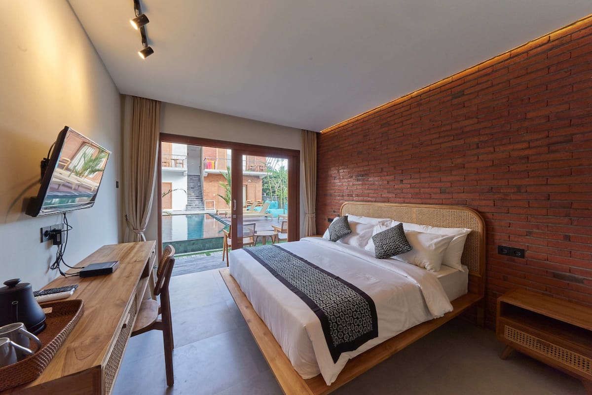 Quarto de hotel moderno com uma cama grande, uma escrivaninha de madeira, televisão e varanda com vista para a piscina.