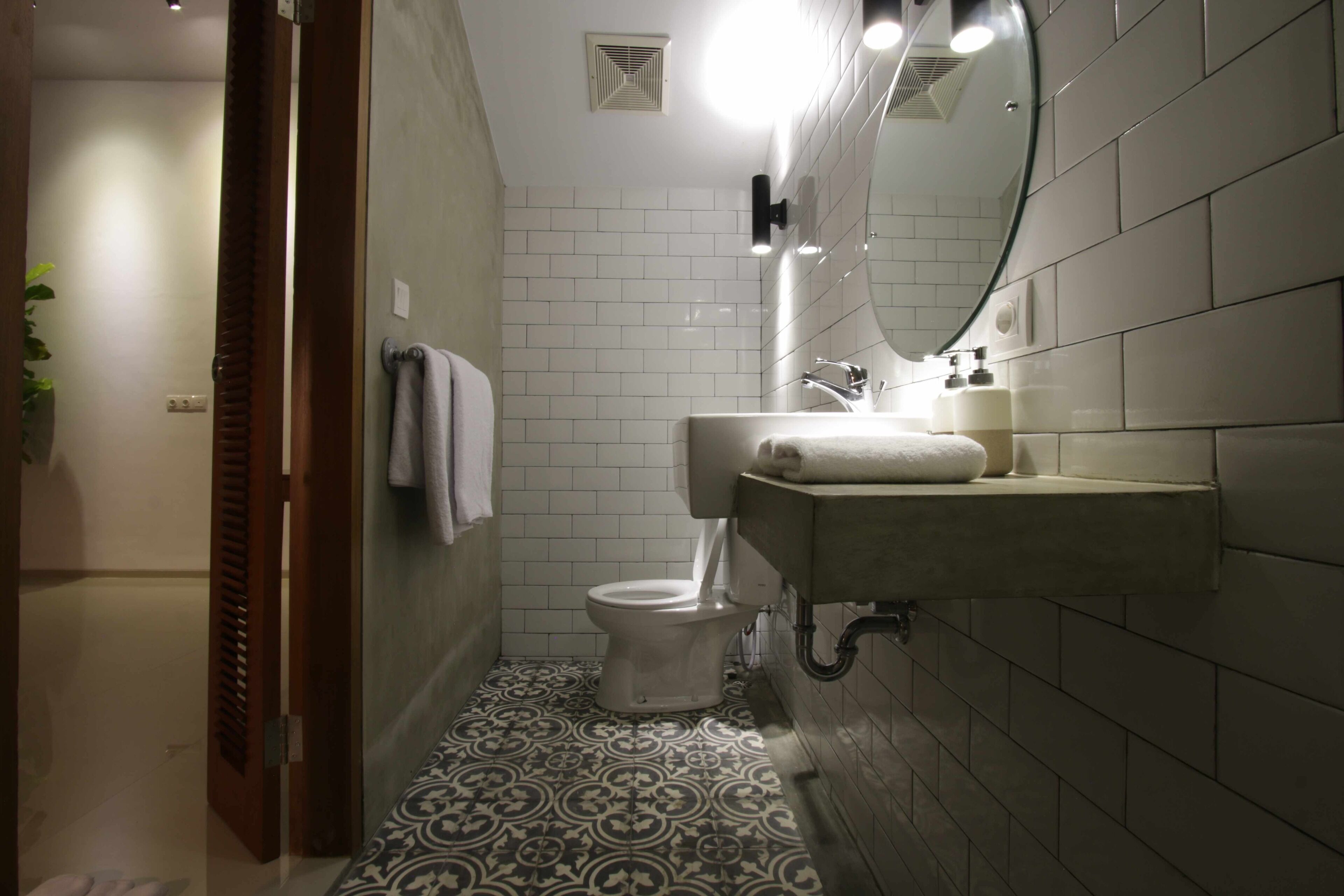 Un baño con inodoro blanco, lavamanos con espejo y baldosas de suelo estampadas.
