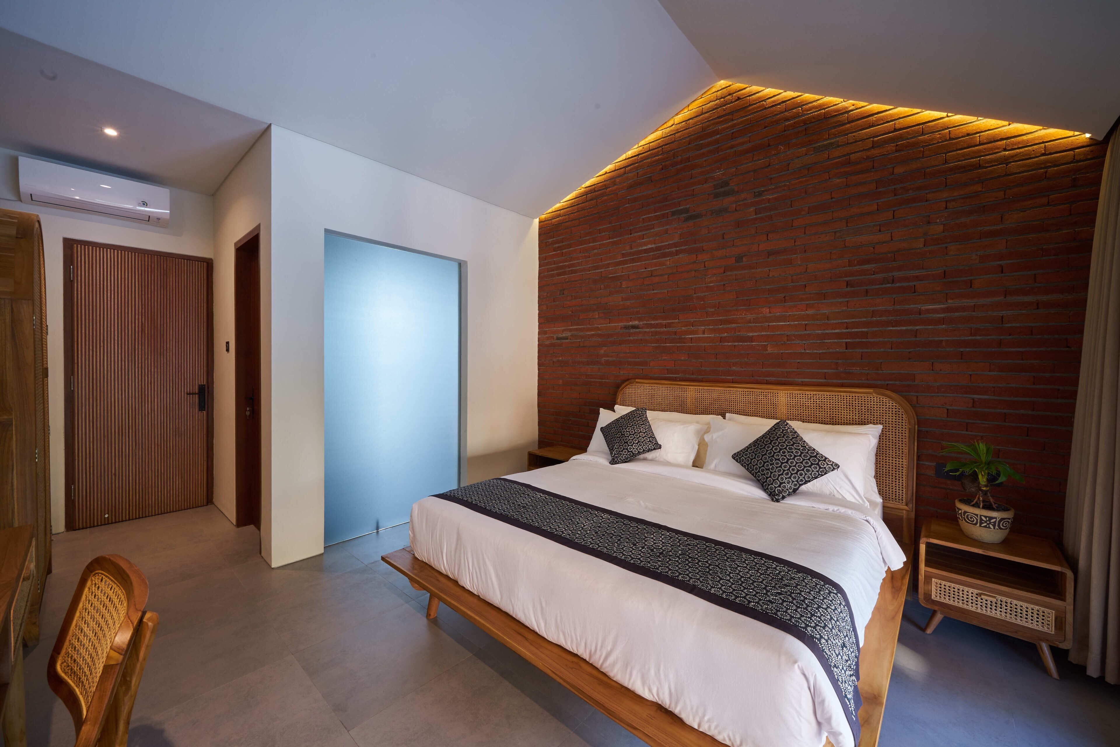 A modern bedroom with a large bed, a brick accent wall, and a small bedside table with a plant.