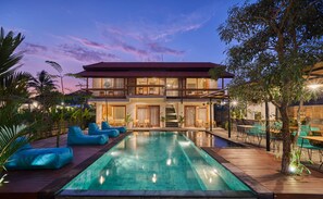 Une maison à deux étages avec une piscine, un espace salon extérieur et un balcon.