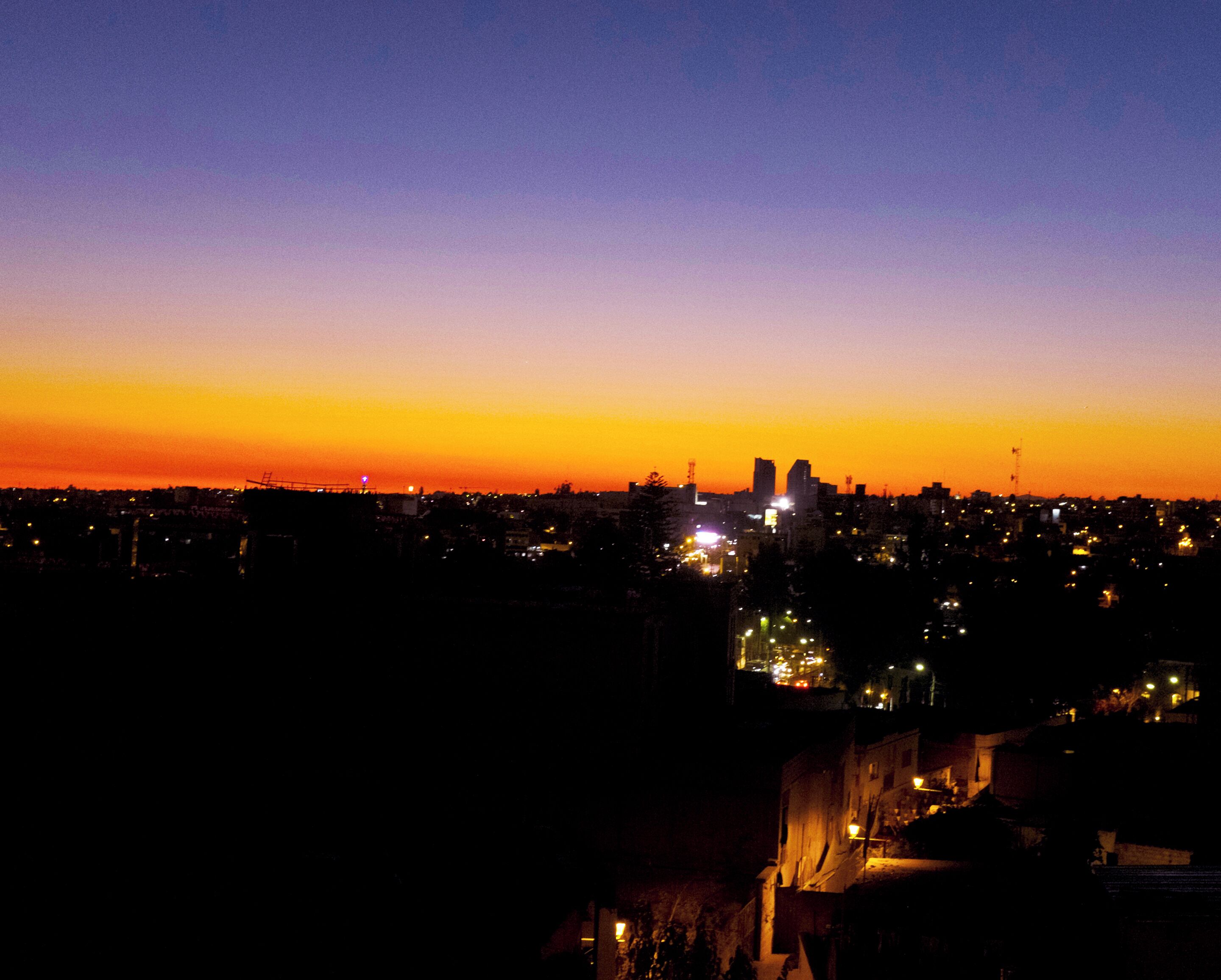 Un paisaje urbano al atardecer con edificios iluminados y un cielo despejado.