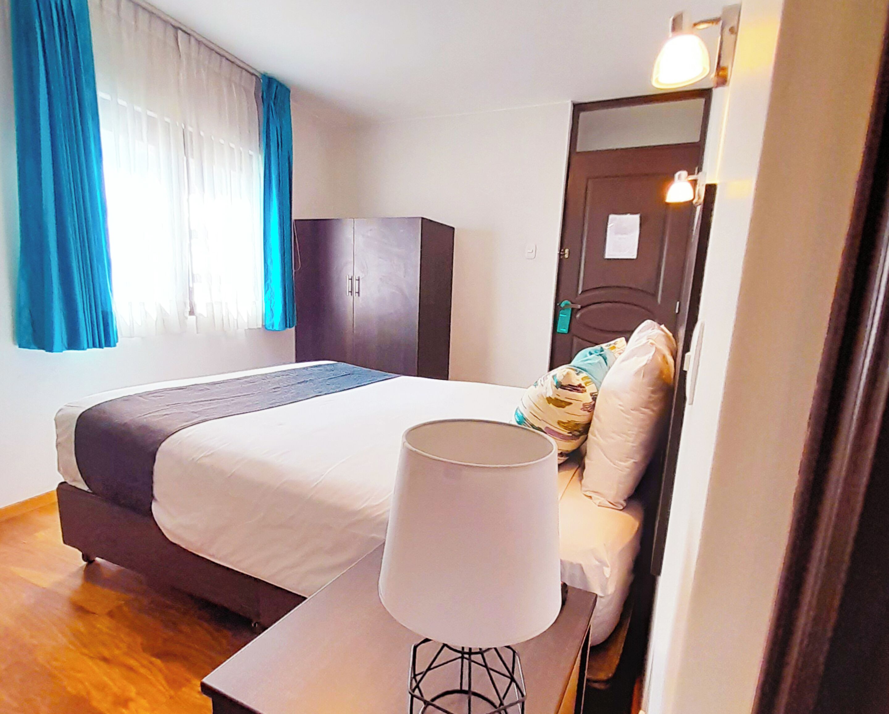 A bedroom with a bed, a bedside table with a lamp, a wardrobe, and a door with a lock.