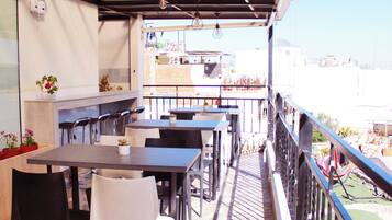 Un área de comedor al aire libre con mesas y sillas, barandilla y vistas panorámicas de la ciudad.