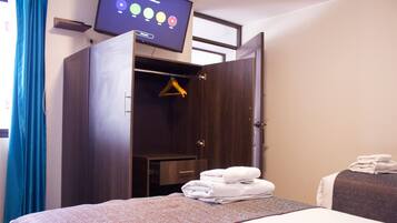 Habitación de hotel con cama, armario, televisión y una pila de toallas.