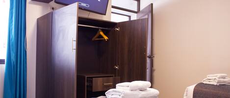 A hotel room with a bed, a wardrobe, a television, and a towel stack.
