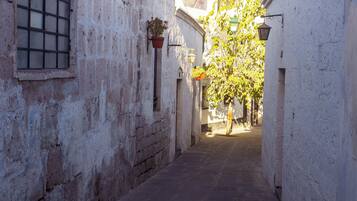 Un estrecho callejón con paredes blancas, una ventana con rejas y una planta en maceta.