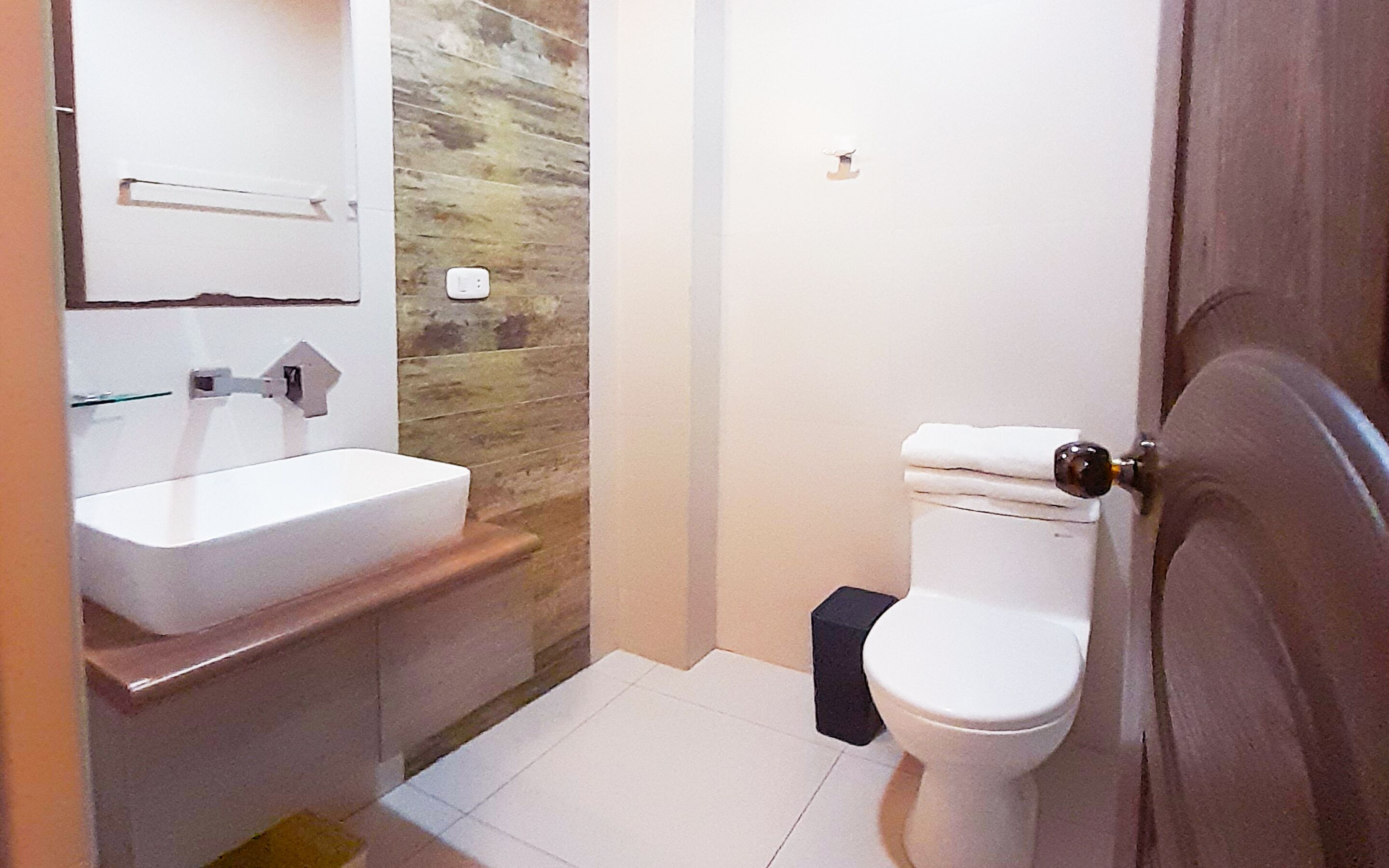 A small bathroom with a white sink, a toilet, and a wooden wall.