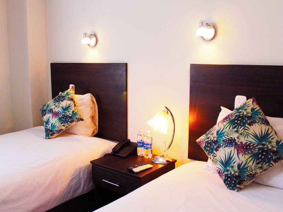 Habitación de hotel con dos camas, cada una con un cojín floral y una mesita de noche con lámpara, teléfono y botellas de agua.
