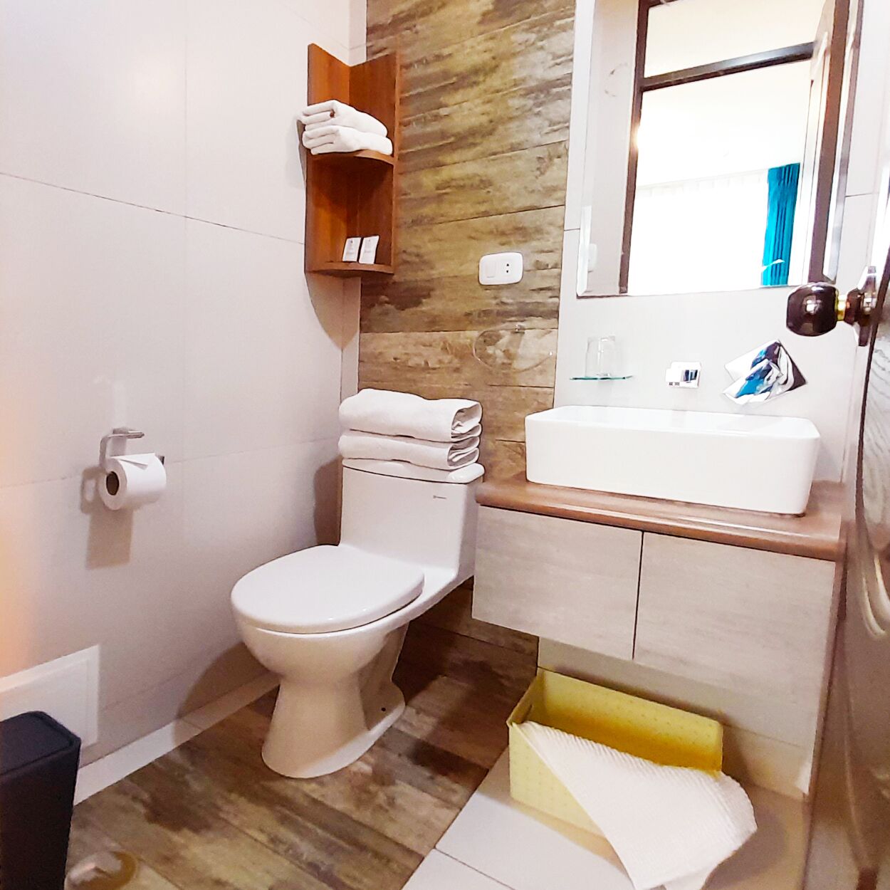 Un baño pequeño con inodoro, lavamanos y un estante de madera con toallas.
