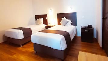Quarto de hotel com duas camas, piso de madeira, uma escrivaninha e uma cadeira.