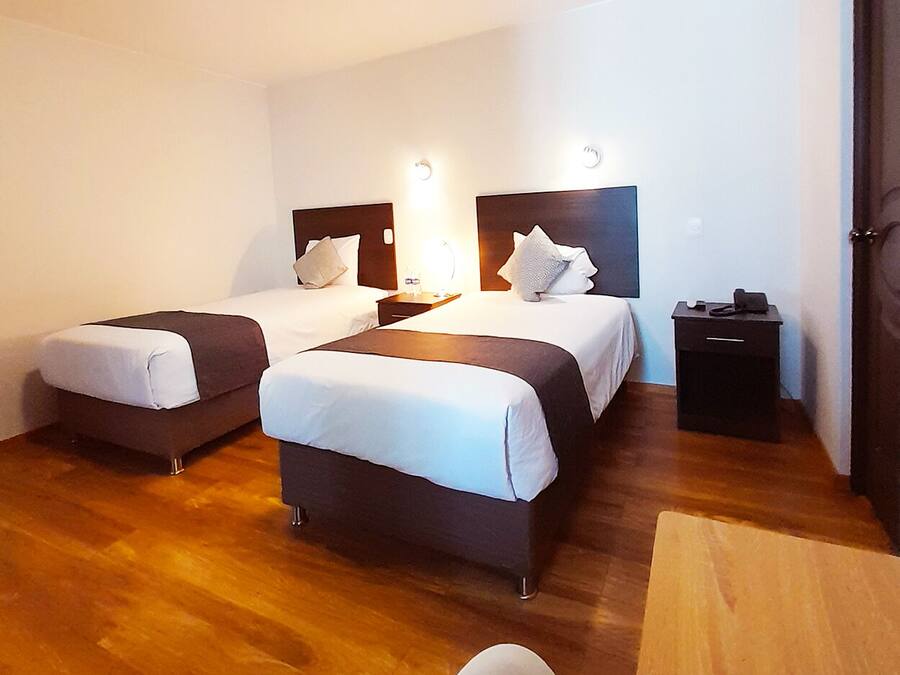 Quarto de hotel com duas camas, piso de madeira, uma escrivaninha e uma cadeira.