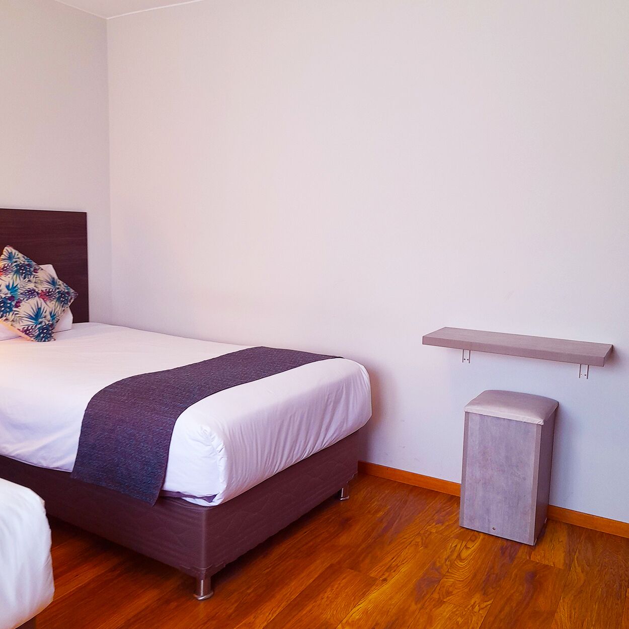 A neatly arranged bedroom with a bed, a bedside table, and a small shelf.