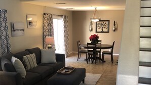 A living room with a dark sofa, a coffee table, and a dining area with a table and chairs. - Beautiful 2 BR Plus Loft, Attached 2 Car Garage, Recently Updated! (Scottsdale)