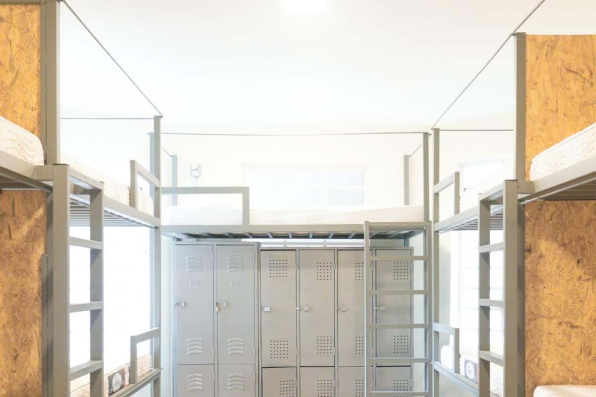 A dormitory room with bunk beds, a wooden floor, and a row of lockers in the center.