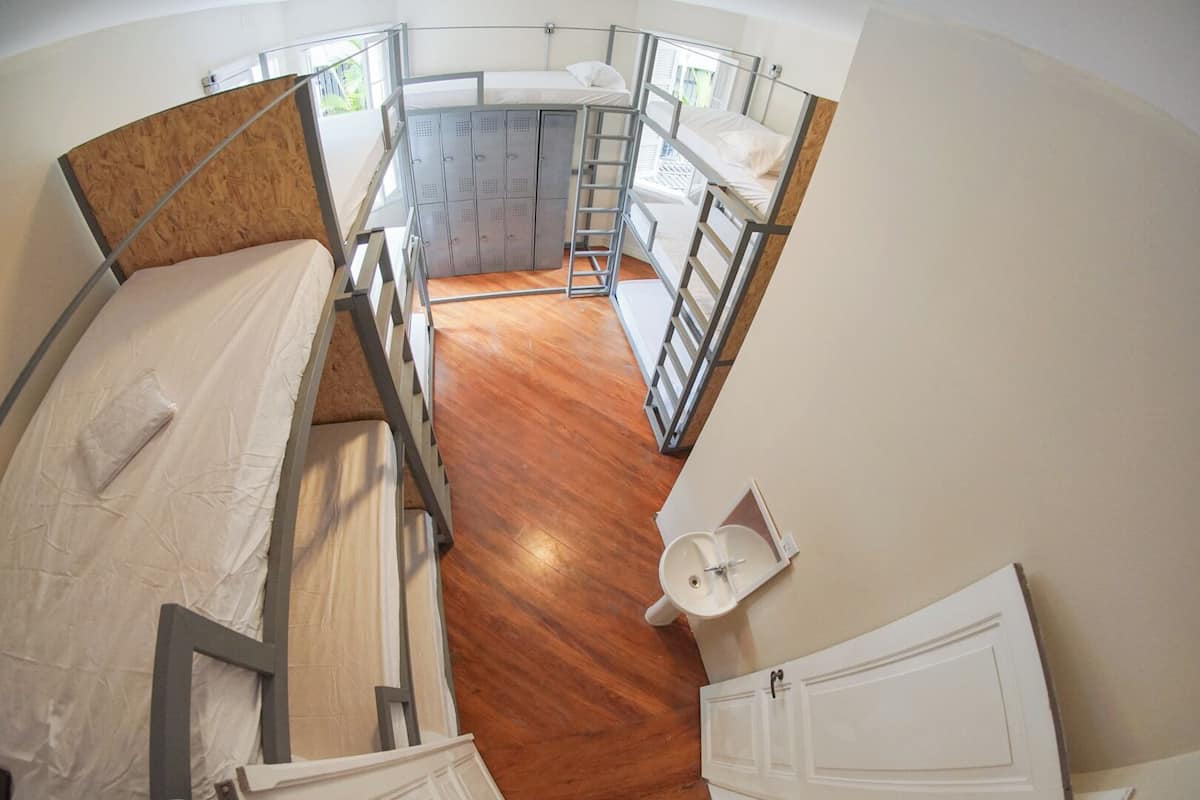 A compact dormitory room with bunk beds, a small bathroom, and a wooden floor.