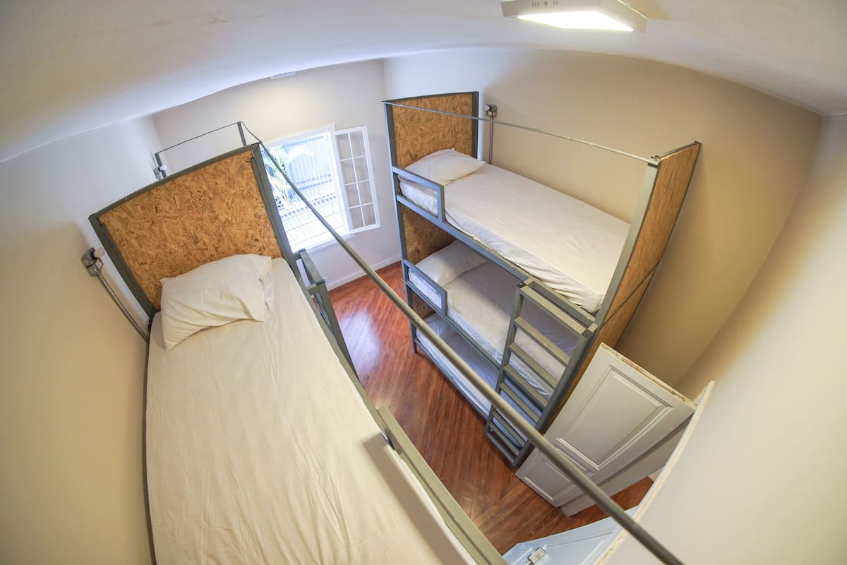 A dormitory room with bunk beds, a window with blinds, and a radiator.