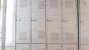 A row of metal lockers with ventilation holes, under a wooden ceiling structure. - Quintal Hostel (São Paulo)
