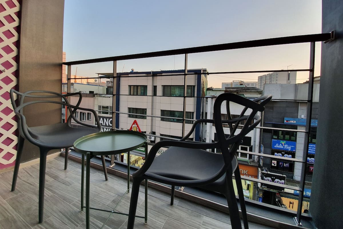 A balcony with two chairs and a small table, overlooking a cityscape with buildings and a sign for 'Sublime Bay'.