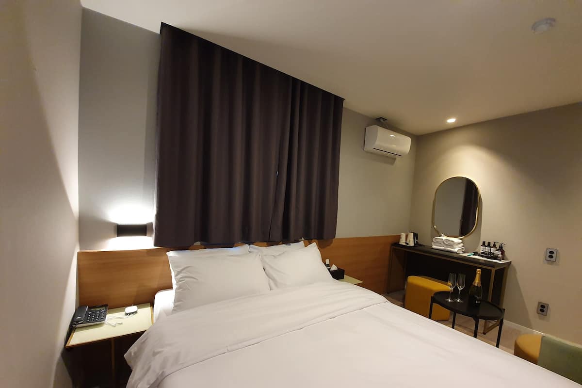 A hotel room with a bed, a desk with a phone, a chair, a mirror, and a small table with toiletries.