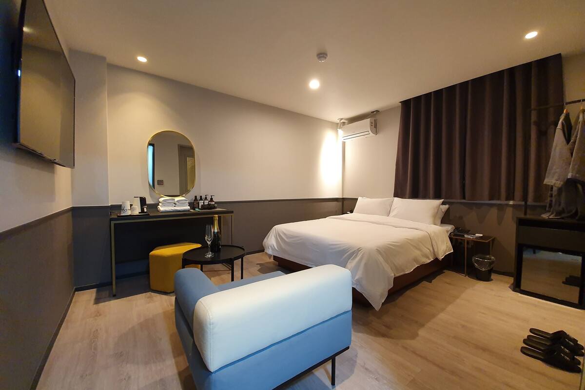 A modern hotel room with a bed, a desk, a chair, and a TV.