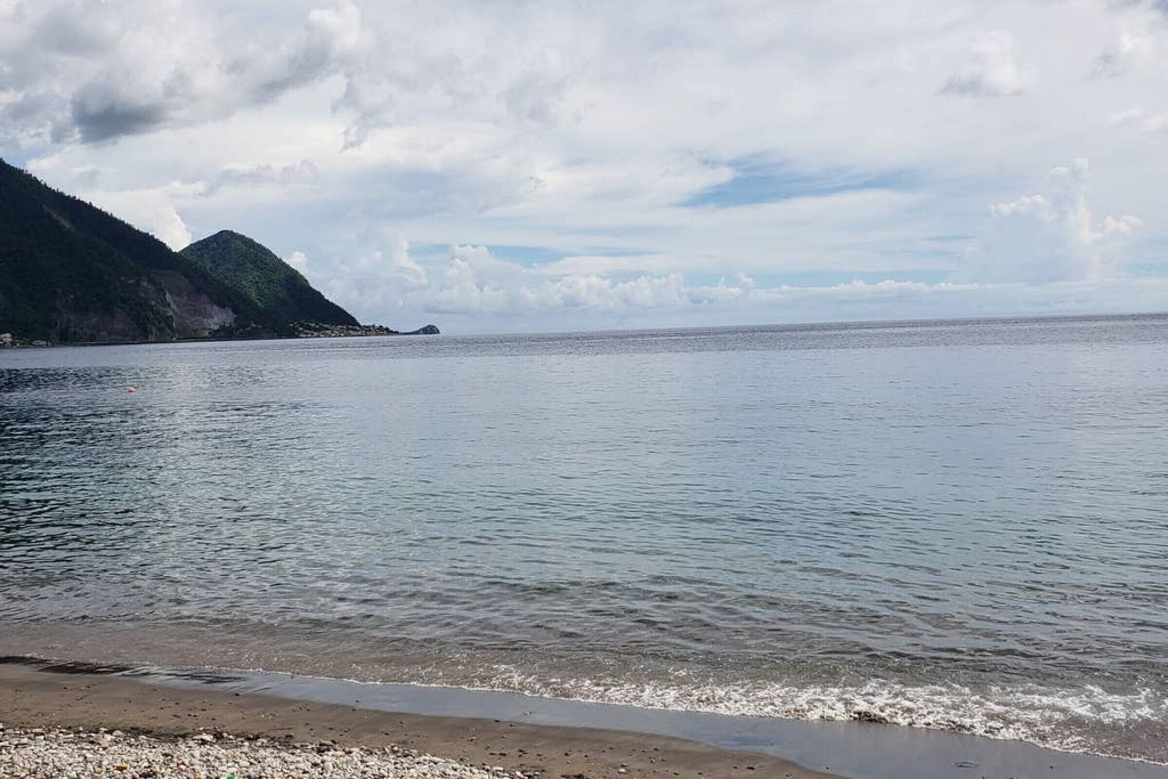 Une mer calme, une plage de galets et une montagne en arrière-plan.