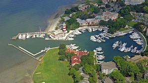 An aerial view of a marina with boats docked, a lighthouse, and surrounding residential buildings. - Egret Point - Large 3BR/3BA - Great Location with Water View and Pool (Hilton Head Island)