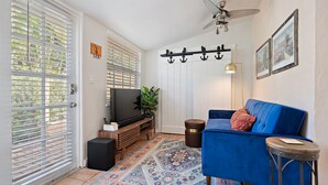 Un salon avec un canapé bleu, un téléviseur, un tapis à motifs et un ventilateur de plafond.