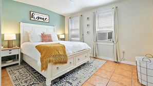 Une chambre à coucher comprenant un lit, des tables de chevet, un ventilateur de plafond et une fenêtre avec des rideaux.