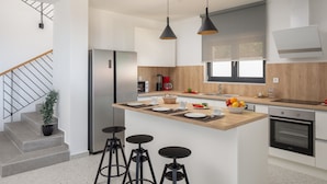 A modern kitchen with a central island, bar stools, a stainless steel refrigerator, a coffee maker, and a built-in oven. - Sun Dance Luxury Villa II (Primošten)