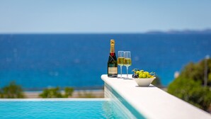 A bottle of Moët & Chandon champagne, two glasses of champagne, and a bowl of grapes on a poolside ledge with a view of the ocean. - Sun Dance Luxury Villa II (Primošten)