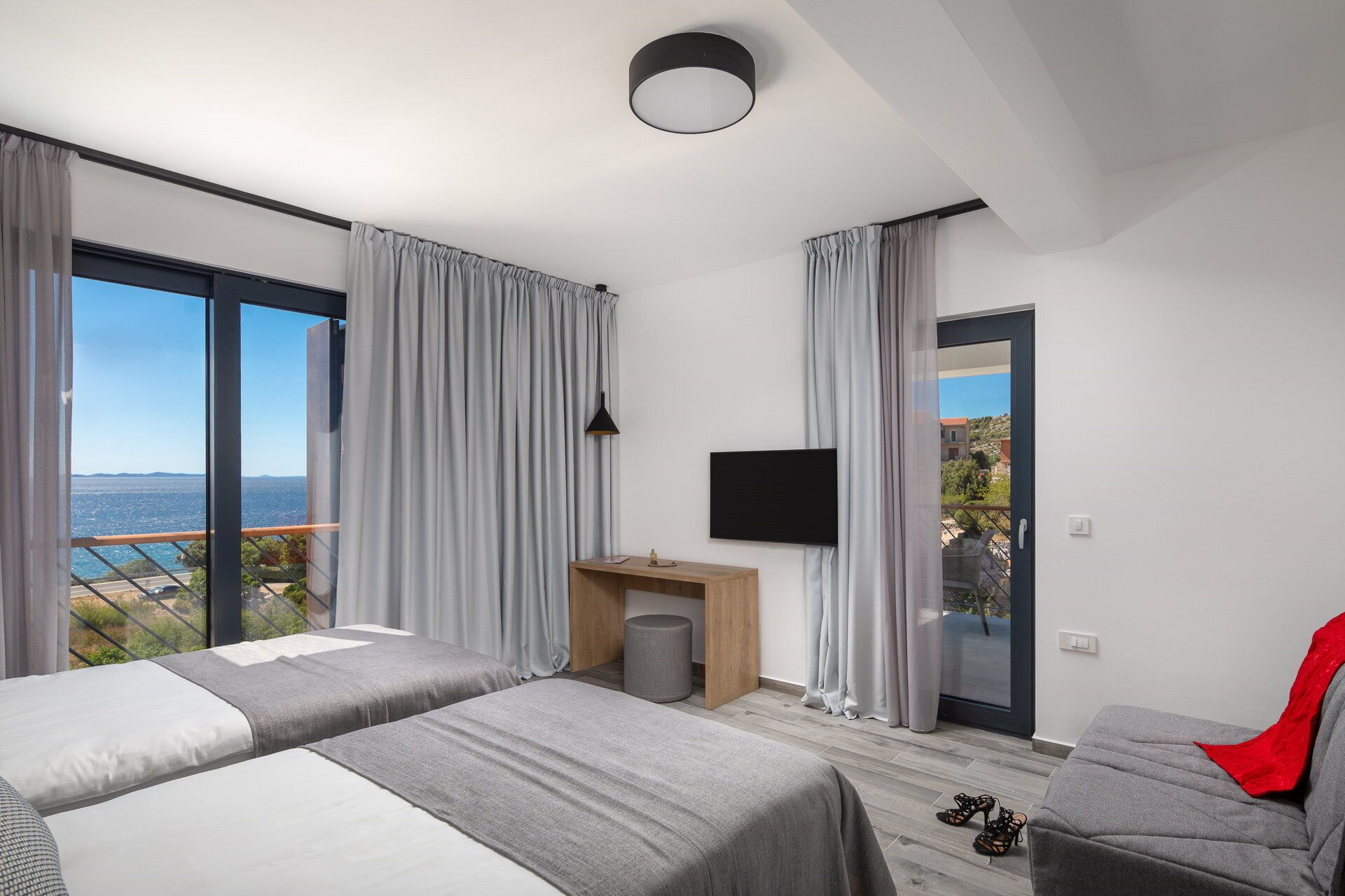 A modern hotel room with two beds, a TV, and a balcony with a view.