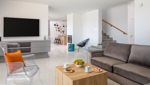 A modern living room with a grey sofa, a wooden coffee table with pastries, and a TV mounted on the wall.