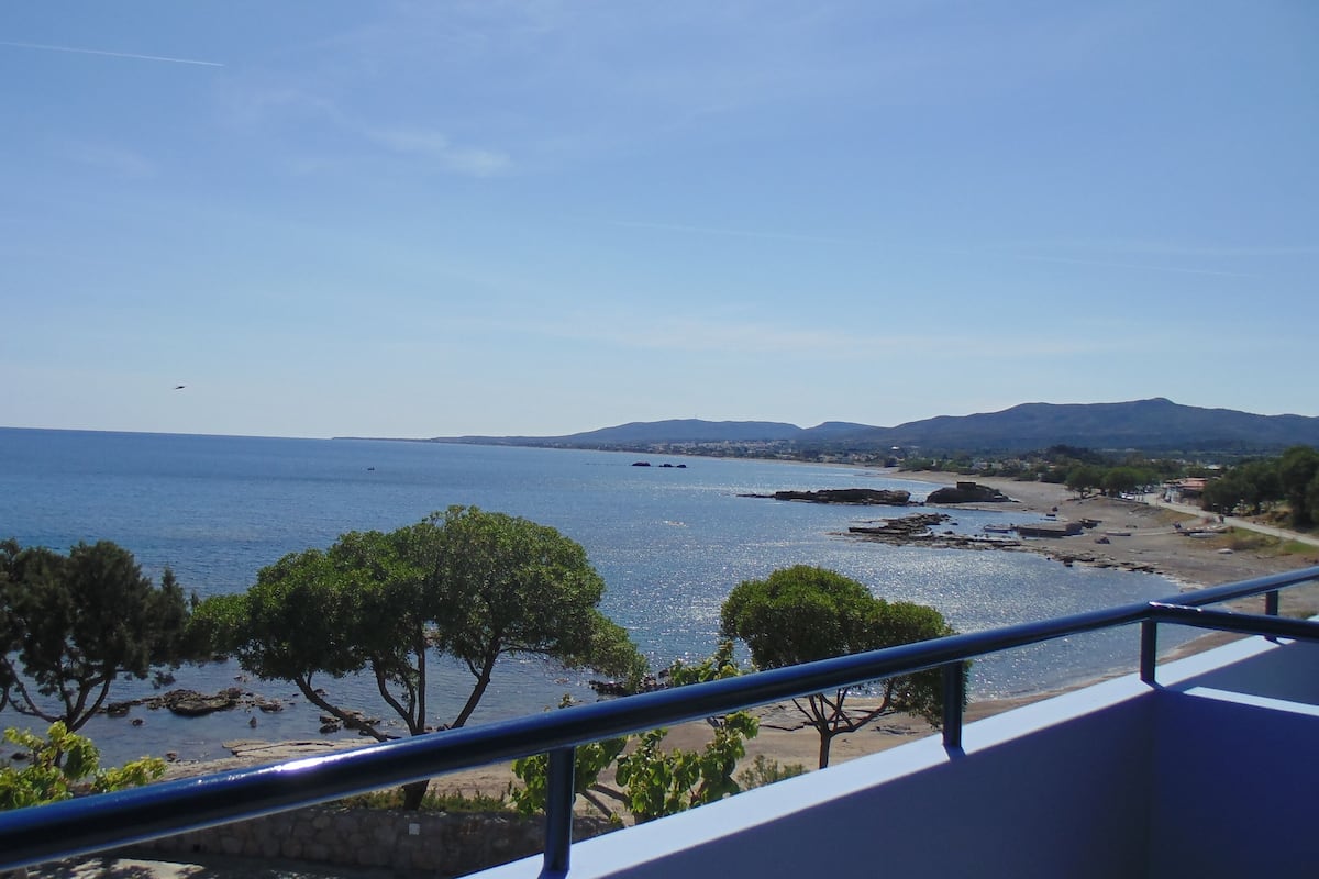 Une vue sur la côte, avec un balcon donnant sur la mer, un rivage rocheux et des montagnes au loin.