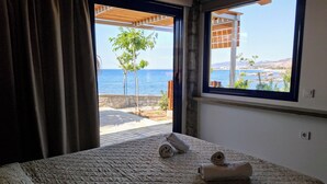 Ein Schlafzimmer mit einem Bett, einem Fenster mit Meerblick und einem teilweise zurückgezogenen Vorhang.