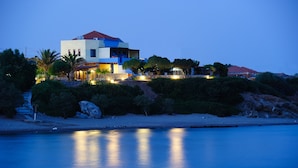 Ein modernes, zweistöckiges Haus mit rotem Dach, das auf einem felsigen Hügel mit Blick aufs Meer liegt.