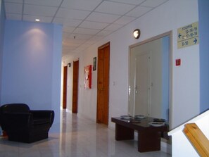 Un pasillo con mostrador de recepción, una silla negra y un cartel que indica la disponibilidad de habitaciones.