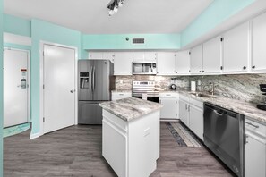 A modern kitchen with white cabinets, a central island, stainless steel appliances, and a marble countertop. - Orange Beach Sea Salt Ocean Views (Orange Beach)