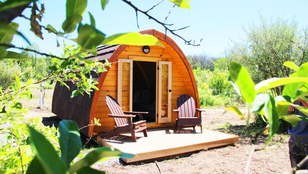 Uma cabana de madeira com varanda, duas cadeiras Adirondack e um deck de madeira.