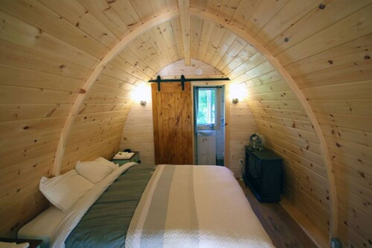 Um quarto de madeira aconchegante, com arco, que inclui uma cama, uma cômoda e uma porta que dá para o exterior.