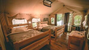 Alojamento tipo tenda com duas camas de madeira, uma pequena mesa e uma janela com vista para o exterior.