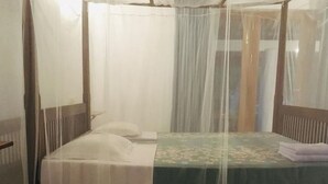 Ein Einzelbett mit Moskitonetz, ein Nachttisch und ein kleiner Teppich.