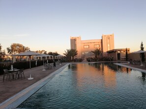 A pool area with outdoor seating and a building with a tower in the background. - Hotel Oasis Palace (Lkheng)