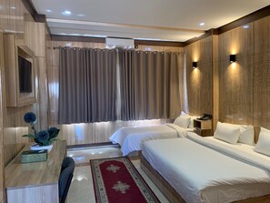 A hotel room with two beds, a desk, a chair, a TV, and a large window with curtains. - Hotel Oasis Palace (Lkheng)