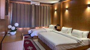 A hotel room with two beds, a desk, a red patterned rug, and a wall-mounted air conditioner. - Hotel Oasis Palace (Lkheng)