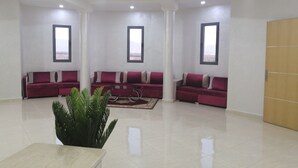 A spacious living room with three red sofas, a coffee table, and a large potted plant. - Hotel Oasis Palace (Lkheng)