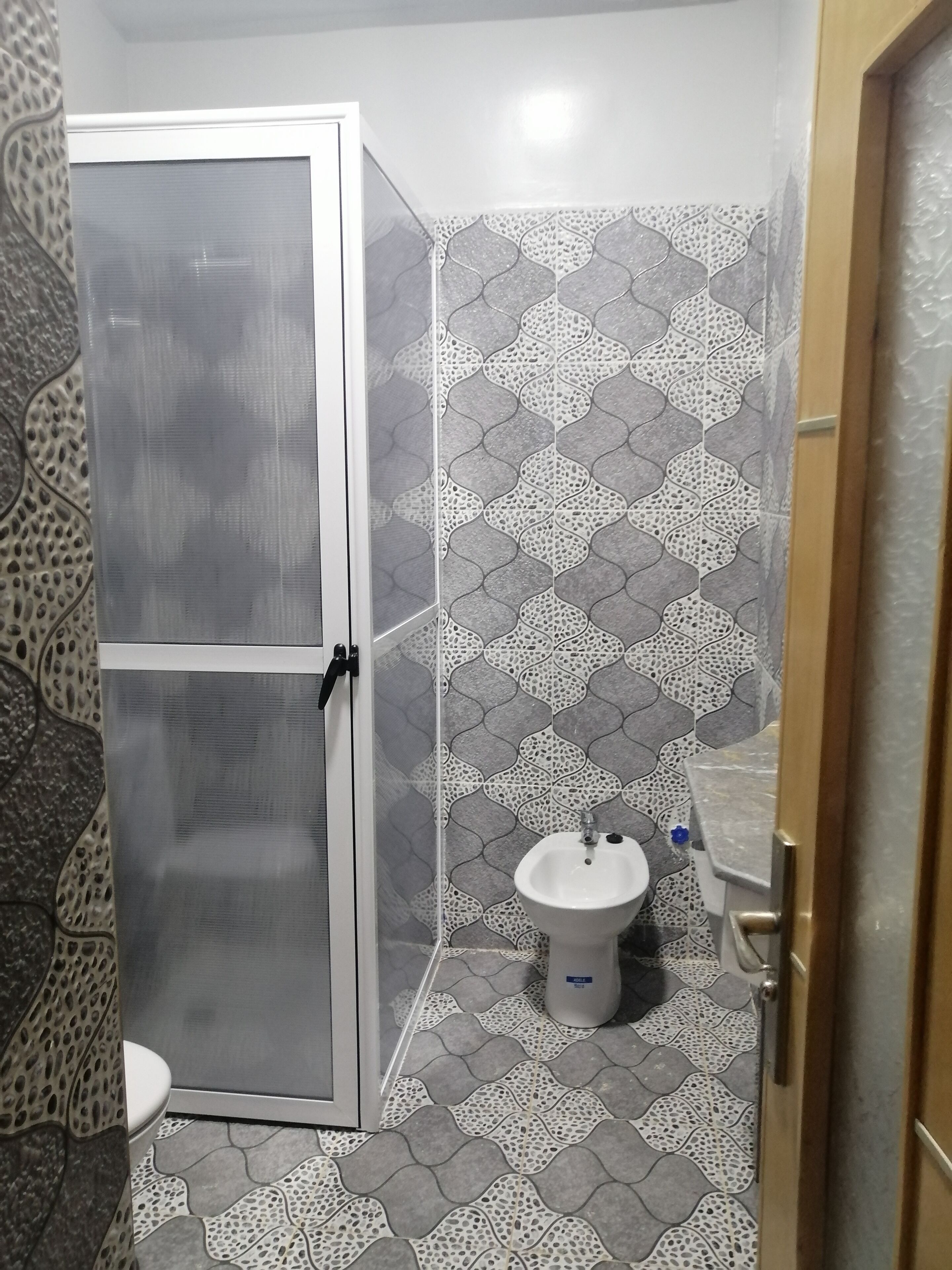 A bathroom with a shower enclosure, a sink, and patterned tiles on the walls and floor.