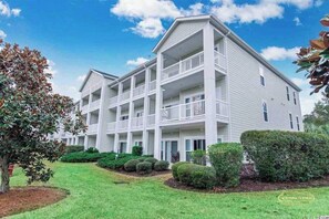A multi-story residential building with balconies, surrounded by well-maintained lawns and hedges.