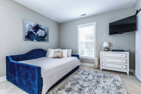 A bedroom with a bed, a dresser, a TV, and a window with blinds.